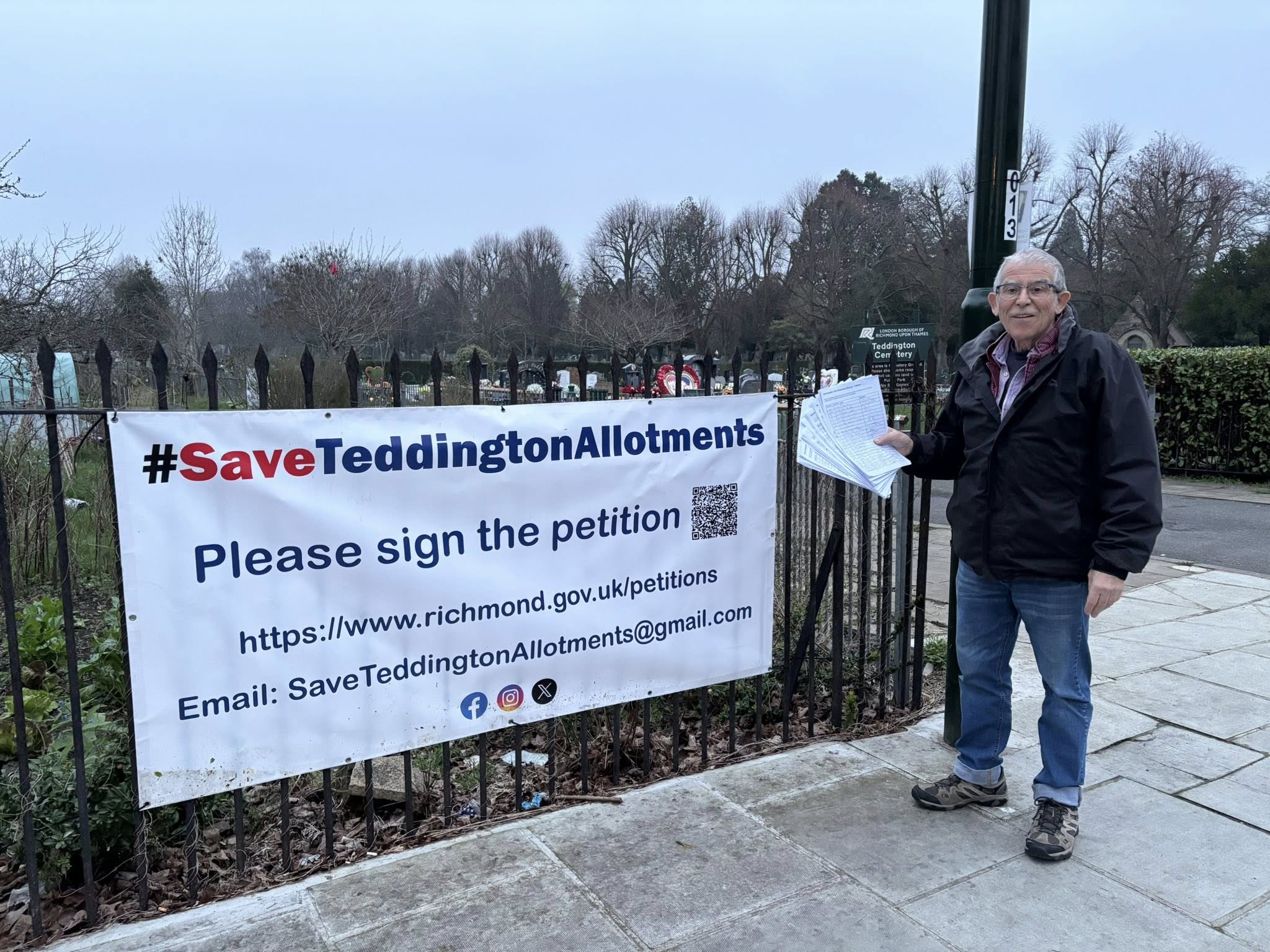 Campaign supporter standing beside the #SaveTeddingtonAllotments banner outside the allotment railings